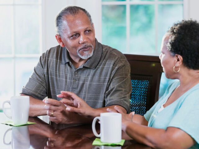 An older couple talking together over coffee at a table.