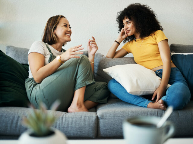 Two people talking together while seated on a sofa.