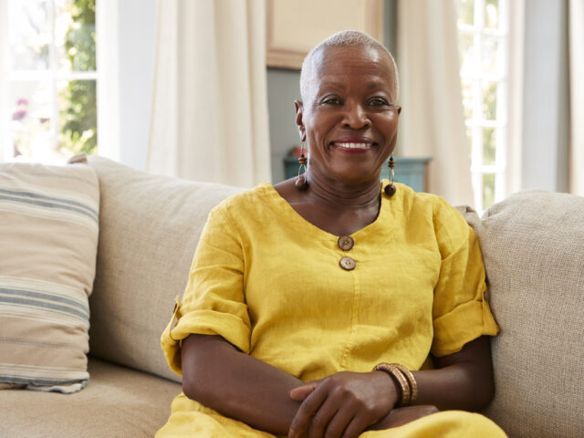 An older woman smiling while seated on a sofa.