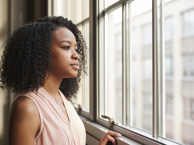 A woman looking thoughtfully out of a window.