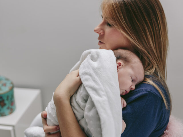 A parent holding a sleeping newborn against their shoulder.